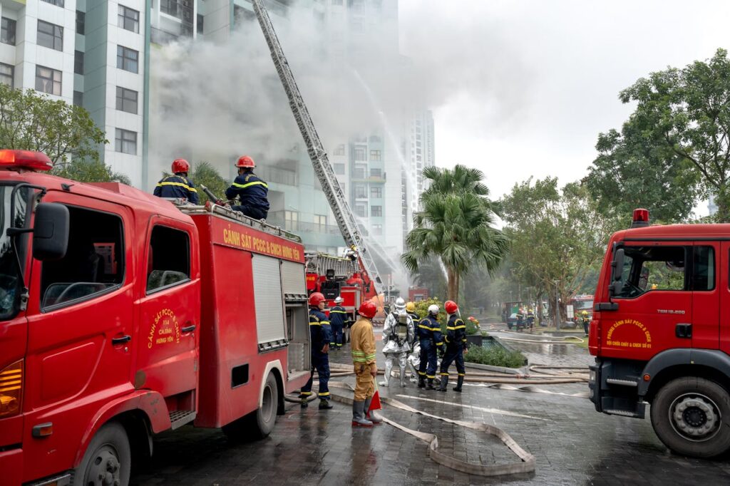 Firefighters in action controlling a fire in a high-rise building, using fire trucks and hoses. Urban setting.