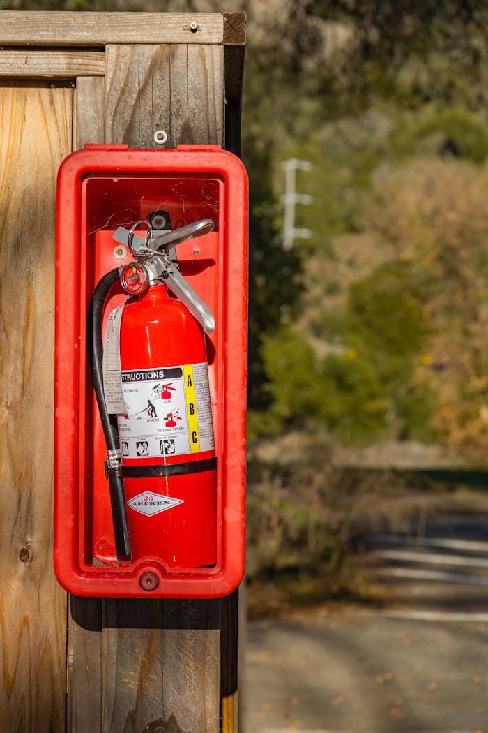 Close-up of a red fire extinguisher mounted outdoors on a wooden post, offering safety and protection.